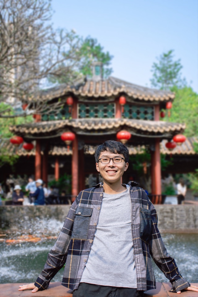 Weicai Long standing in front of a traditional Chinese pavilion